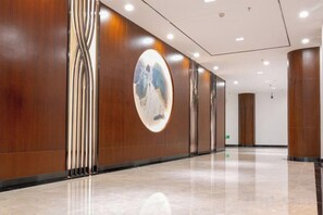 A hallway with wooden paneling, a circular wall art piece, and a polished floor. - WEISELECT MengZi Tian Yuan Hotel (Honghe)