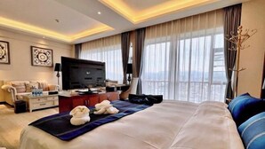A hotel room with a large bed, a desk with a flat-screen TV, a sofa, and a view of the city. - WEISELECT MengZi Tian Yuan Hotel (Honghe)