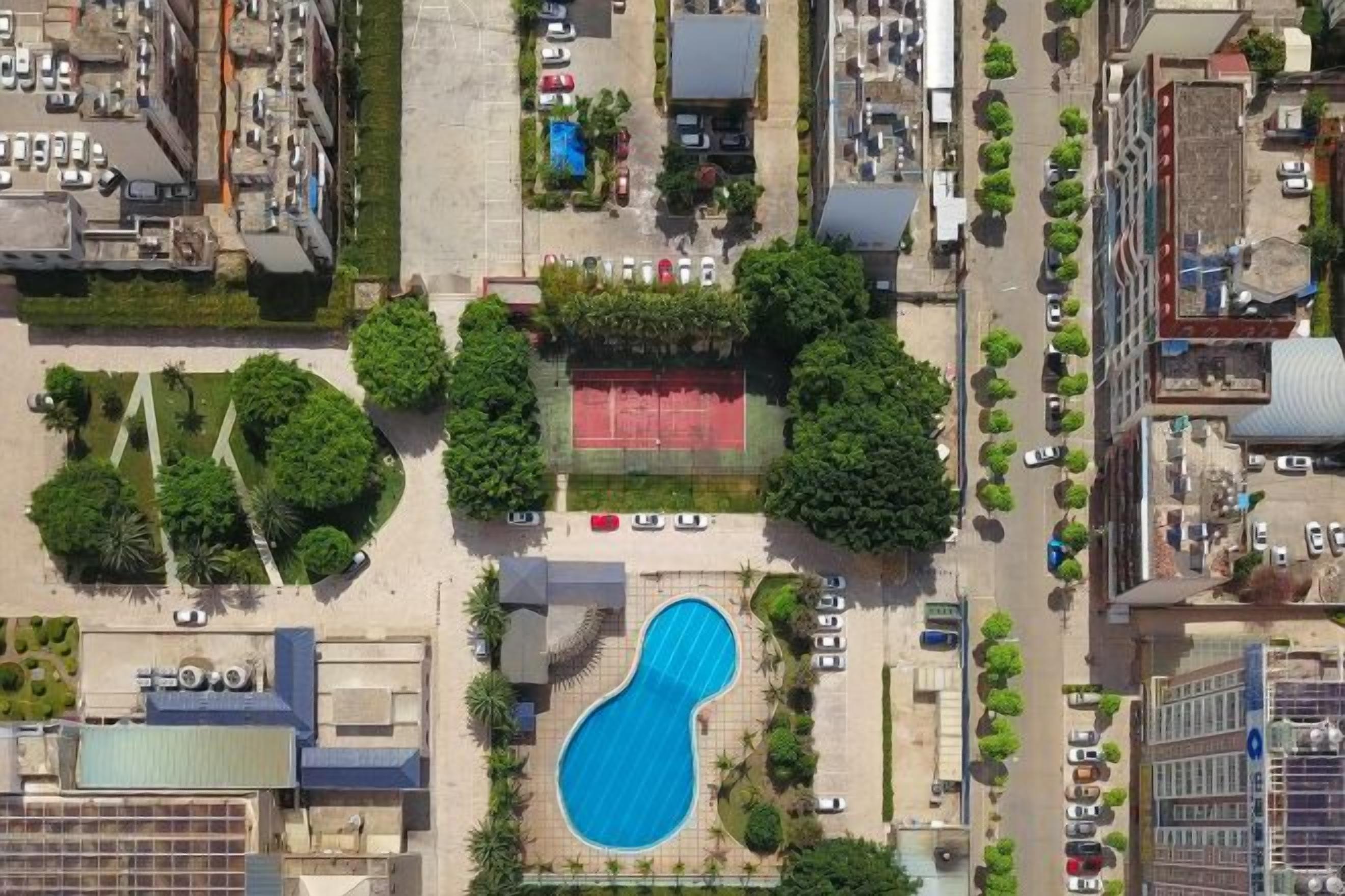 An aerial view of a residential area with a swimming pool surrounded by trees and a tennis court.
