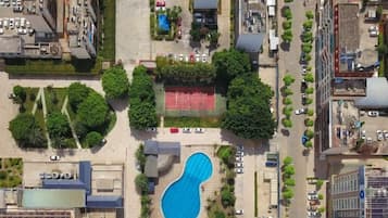 An aerial view of a residential area with a swimming pool surrounded by trees and a tennis court.