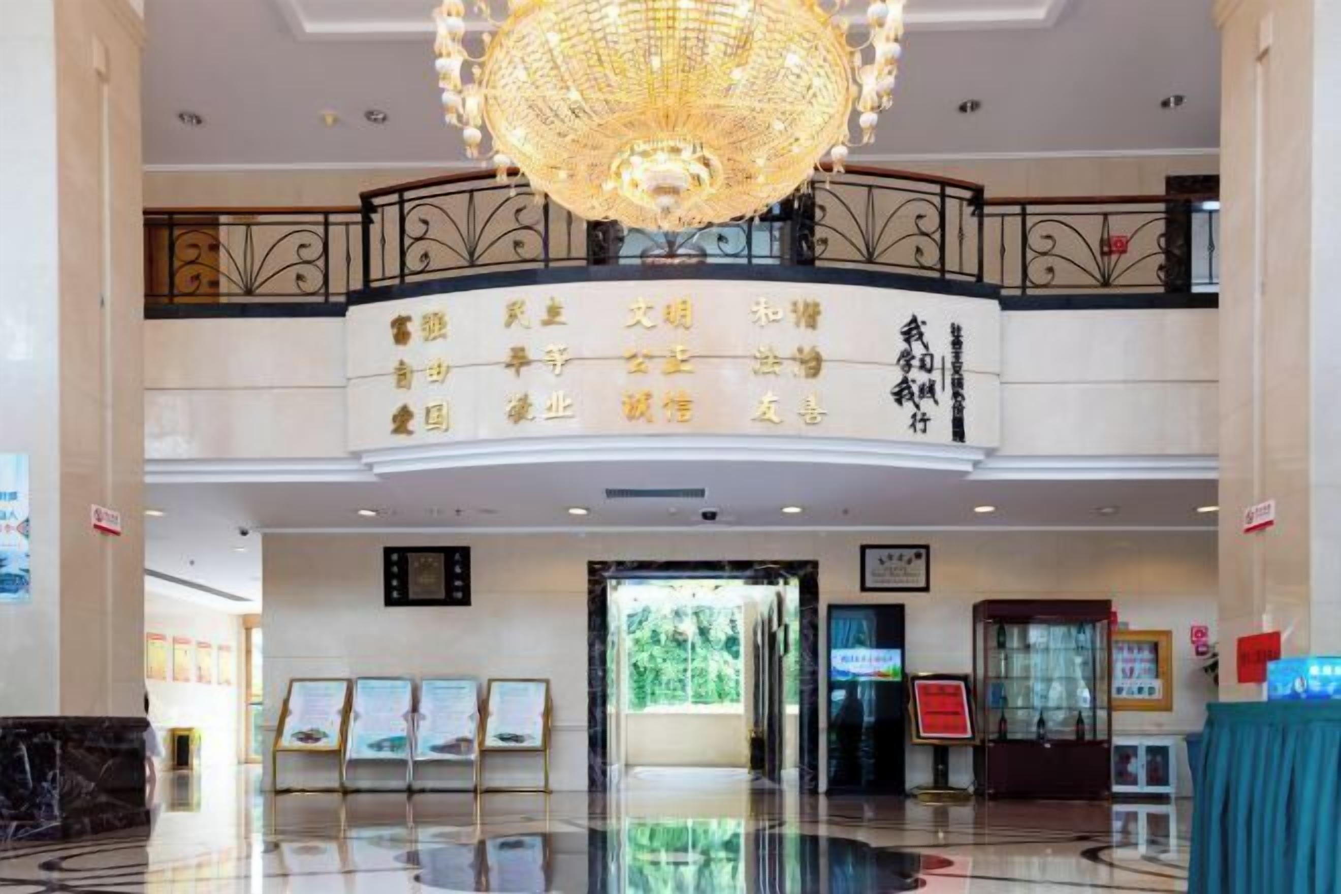 A hotel lobby with a chandelier, a reception desk, and a signboard with text.