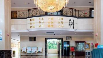 A hotel lobby with a chandelier, a reception desk, and a signboard with text.
