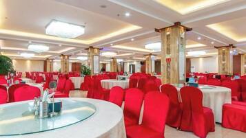 A banquet hall with round tables, red chairs, and a high ceiling with recessed lighting.