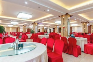 Un salón de banquetes con mesas redondas, sillas rojas y un techo alto con iluminación empotrada.