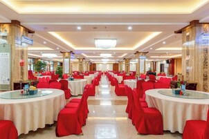 A banquet hall with round tables and red chairs, arranged in rows.