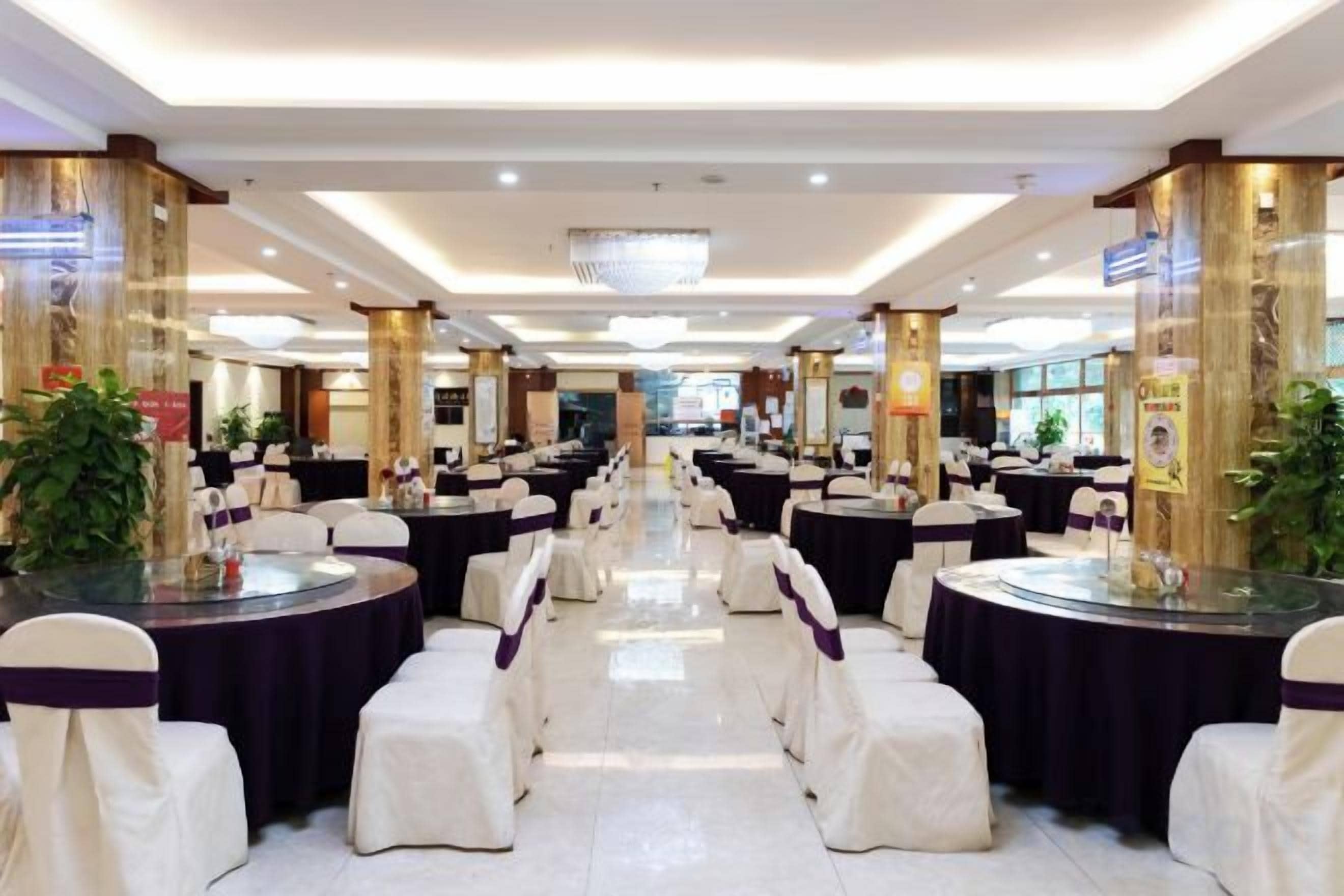 A banquet hall with round tables and chairs, a chandelier, and decorative columns.