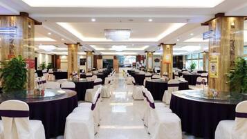 A banquet hall with round tables and chairs, a chandelier, and decorative columns.
