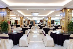 Un salón de banquetes con mesas y sillas redondas, una araña y columnas decorativas.