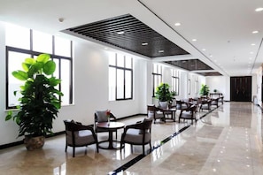 Un amplio vestíbulo de hotel con una larga recepción, varias zonas de estar y grandes ventanales.