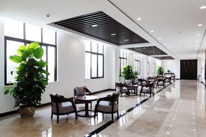 Un amplio vestíbulo de hotel con una larga recepción, varias zonas de estar y grandes ventanales.