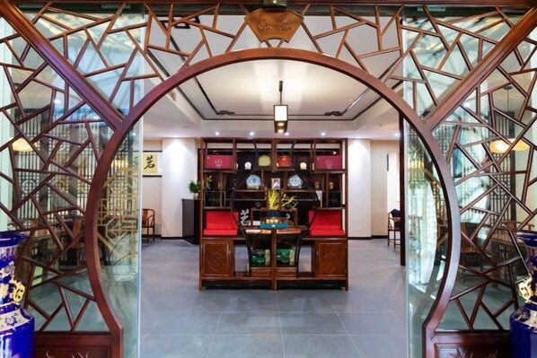 A traditional Chinese-style interior with a central table and red cushions, surrounded by glass partitions with geometric patterns.