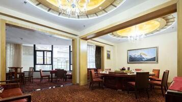 A hotel lobby with a dining area, a chandelier, and a mountain painting on the wall.