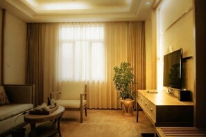 A living room with a sofa, a coffee table, a TV, a potted plant, and a window with curtains. - Fliport Garden Hotel Lhasa (Laha)