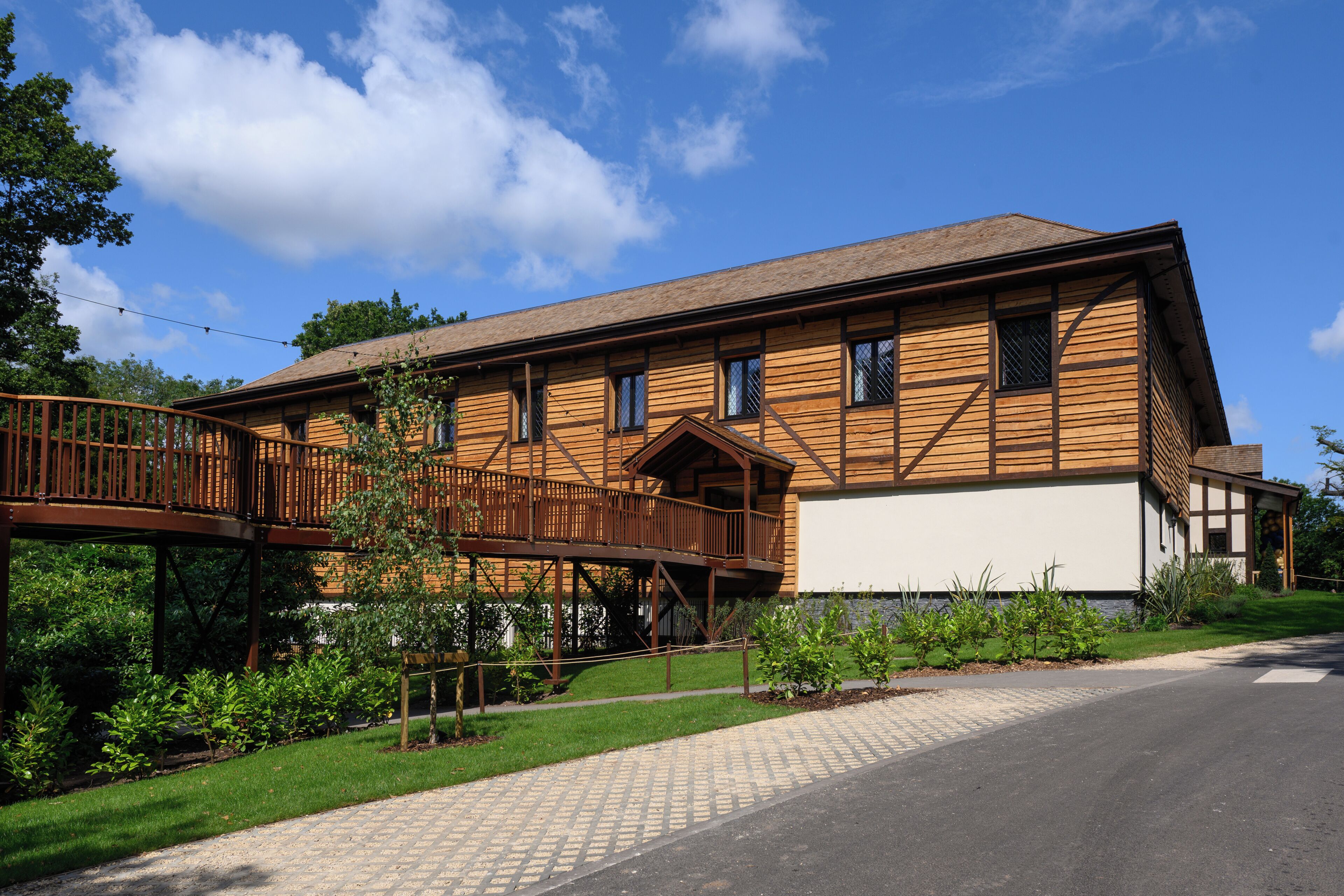 A two-story wooden building with a balcony, a stone foundation, and a paved driveway.
