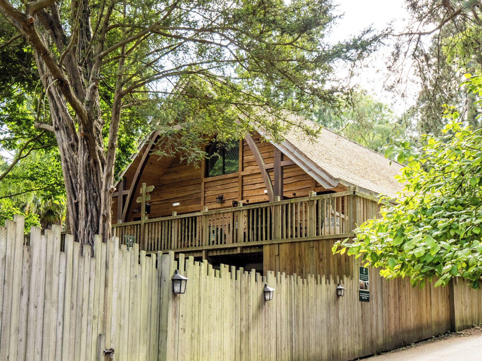 A wooden cabin with a balcony, surrounded by a wooden fence and trees.