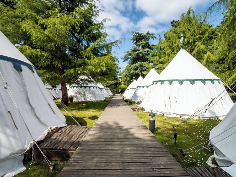 A pathway leading to white tents with green trim, surrounded by trees.