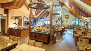 A spacious dining area with wooden tables and chairs, a buffet counter with various food items, and a drinks station. -  Warwick Castle Hotel and Knight's Village (Warwick)