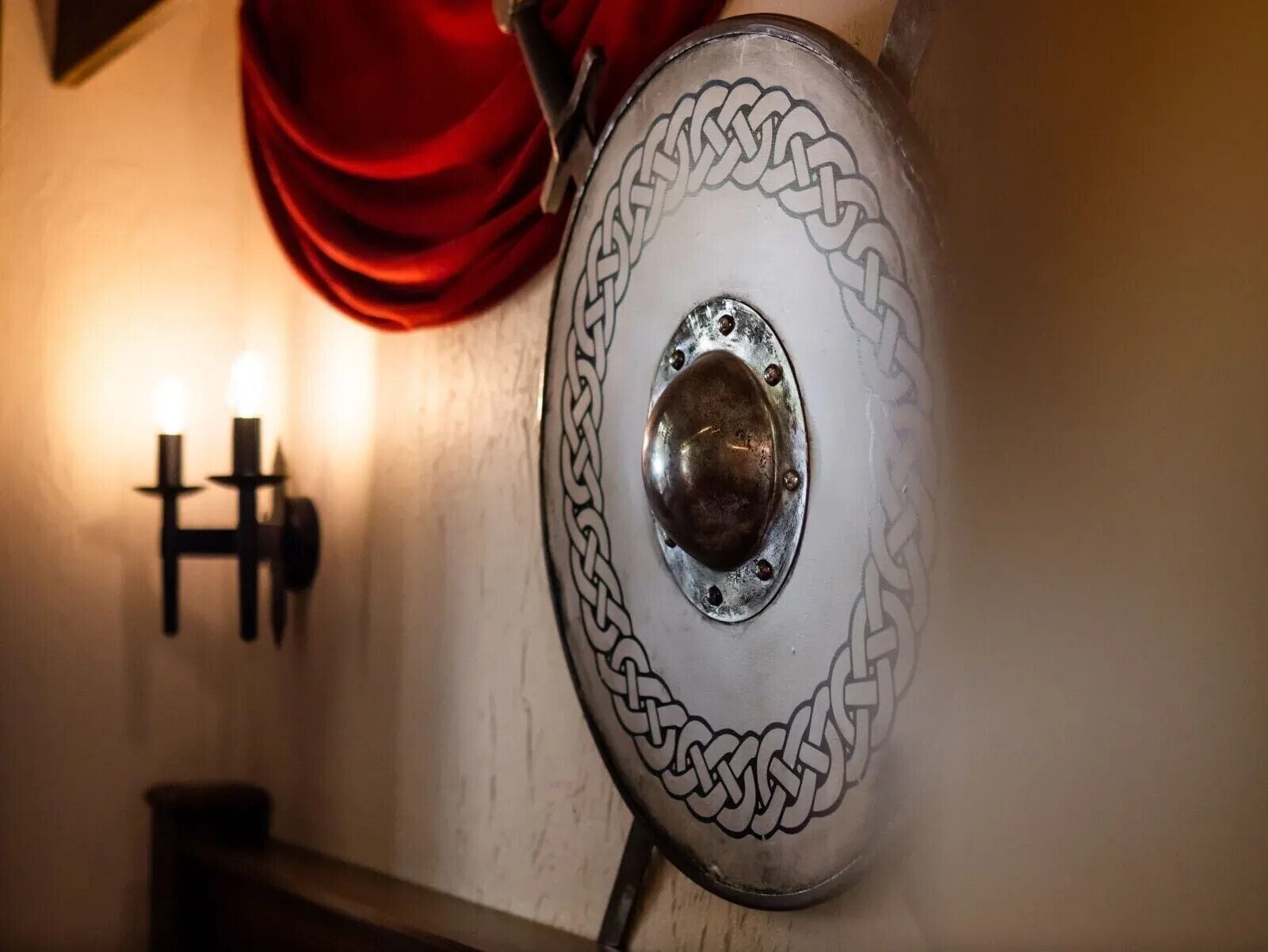 A shield with a chain design, a wall-mounted light fixture, and a red curtain.