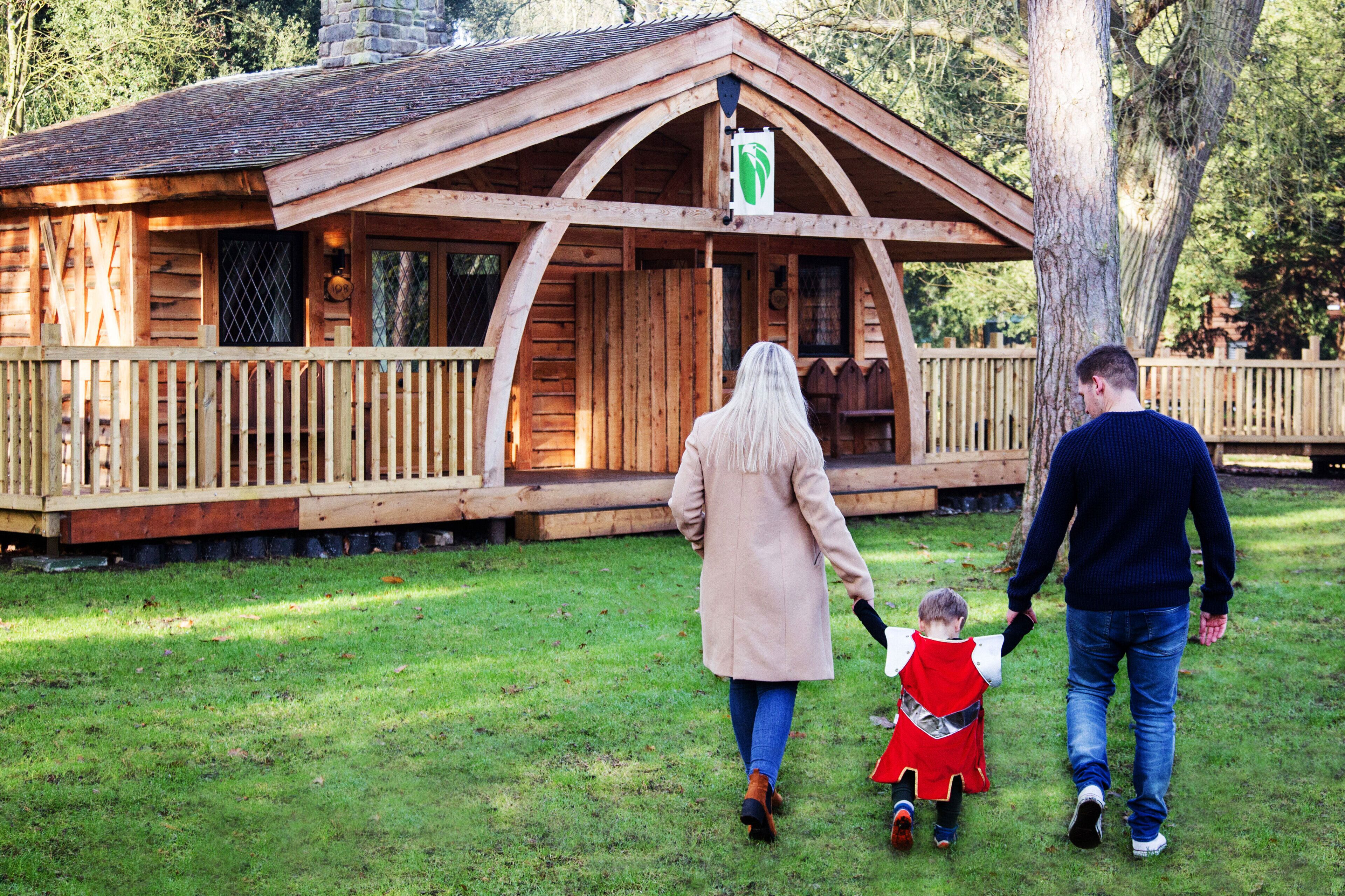 A wooden cabin with a porch, surrounded by grass and trees.