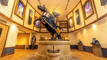 Um lobby com uma estátua central de um cavaleiro a cavalo, quadros nas paredes e um balcão de recepção com um computador.