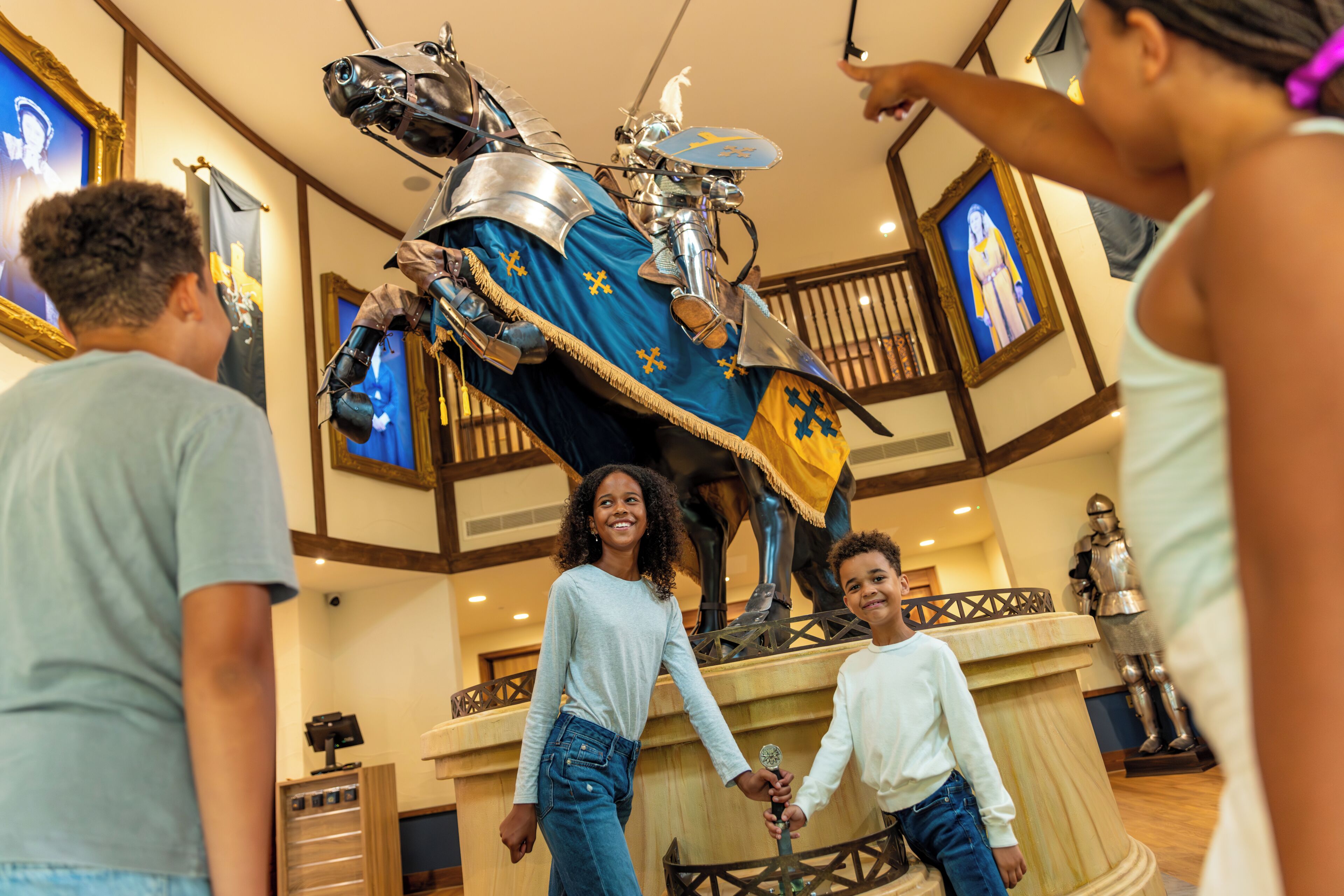 Un gruppo di persone in una hall con una grande statua di un cavaliere e uno sfondo a tema medievale.