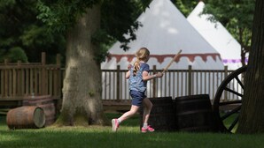 A child playing with a toy sword in a park with a white tent and wooden barrels in the background. -  Warwick Castle Hotel and Knight's Village (Warwick)