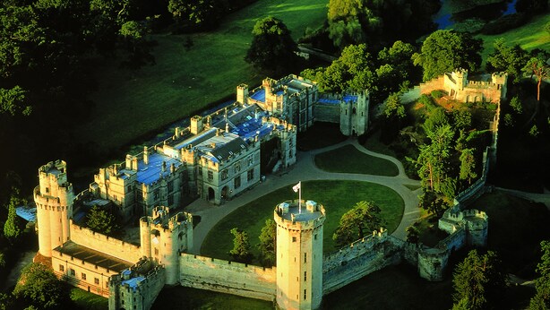 An aerial view of a castle with multiple towers, a central courtyard, and surrounding greenery. -  Warwick Castle Hotel and Knight's Village (Warwick)