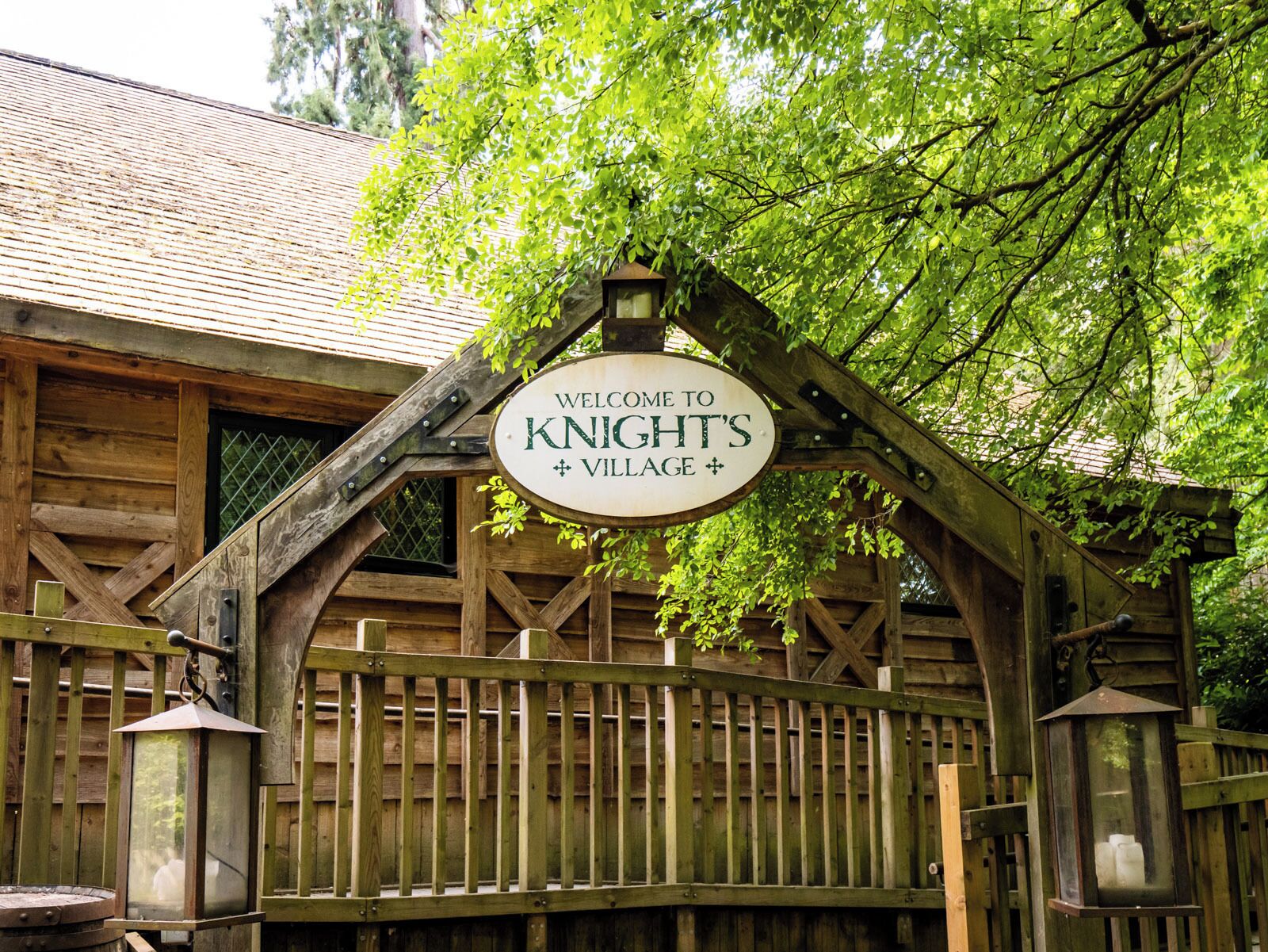 Une pancarte en bois portant l’inscription « Bienvenue au village de Knight » est accrochée au-dessus d’un portail en bois rustique.