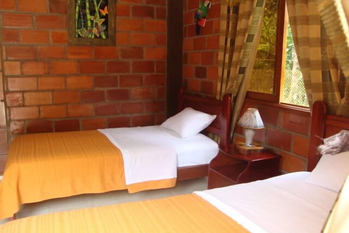 Une chambre avec deux lits, un mur en briques, une fenêtre avec des rideaux et une petite table avec une lampe.