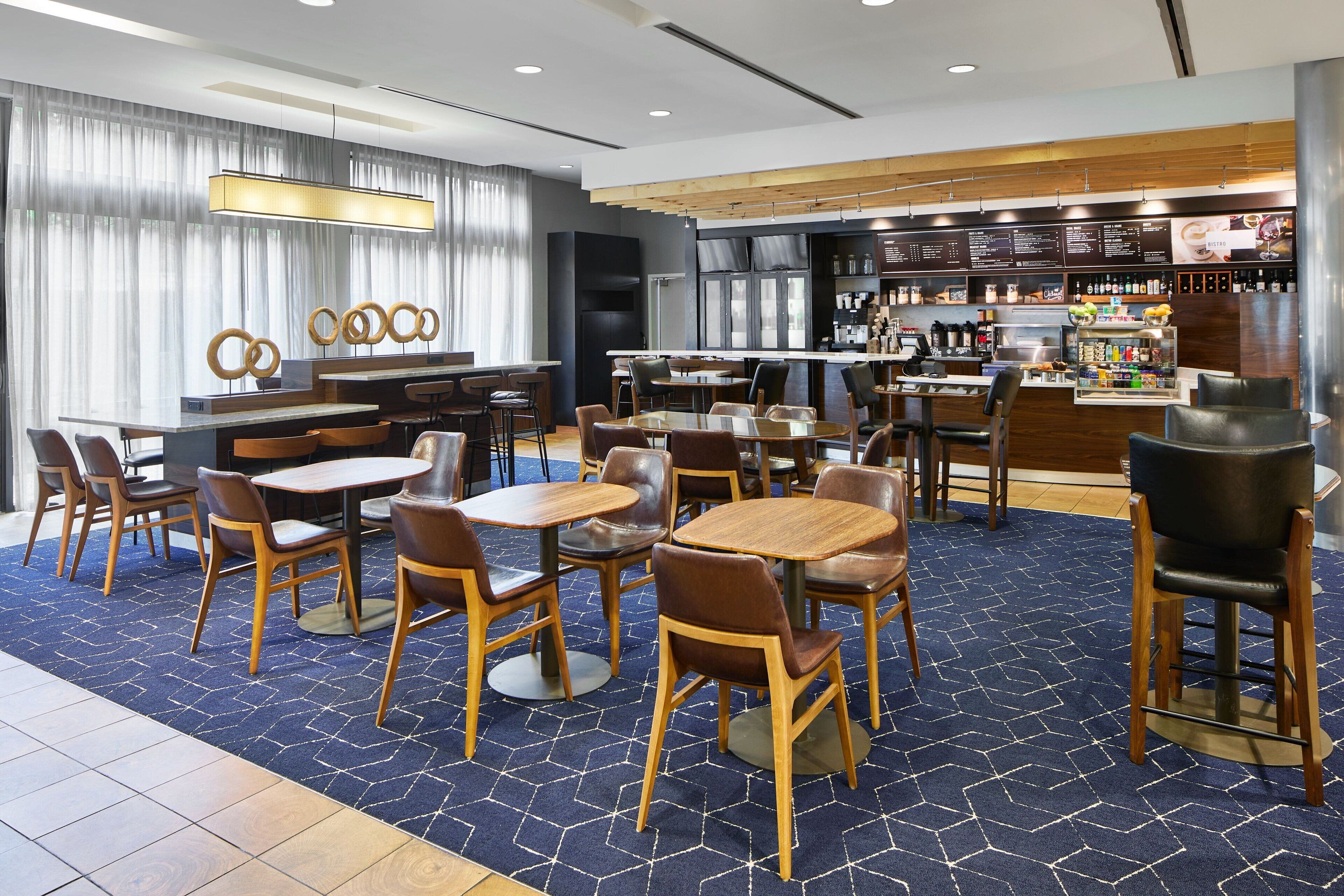 A modern restaurant with wooden tables and chairs, a bar area, and a menu display.