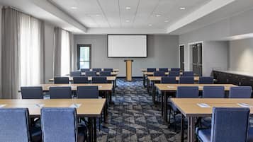 A conference room with a large screen, multiple tables, and chairs arranged for meetings.