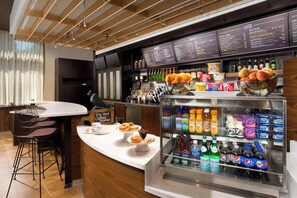 A modern cafe with a counter, seating area, menu boards, and a refrigerated display with beverages and snacks. - Courtyard Atlanta NE/Duluth Sugarloaf (Duluth)