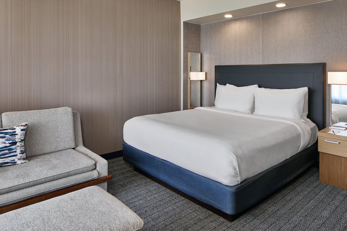 A hotel room with a bed, a sofa, a nightstand, and a mirror.