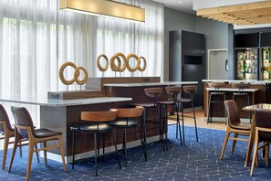 A modern bar area with a wooden counter, bar stools, and a large screen. - Courtyard Atlanta NE/Duluth Sugarloaf (Duluth)