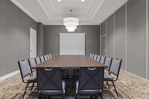 A conference room with a long table, chairs, a projector screen, and a ceiling light fixture. - Hilton Garden Inn Nashville Brentwood (Brentwood)
