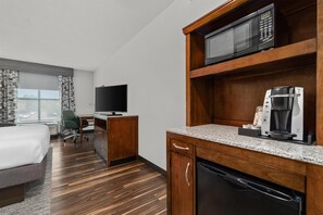 Ein Hotelzimmer mit einem Bett, einem Schreibtisch, einem Fernseher, einer Mikrowelle, einer Kaffeemaschine und einem Geschirrspüler.