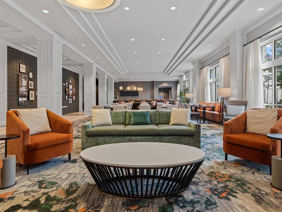 A spacious lobby with a green sofa, orange armchairs, a central coffee table, and a patterned carpet.