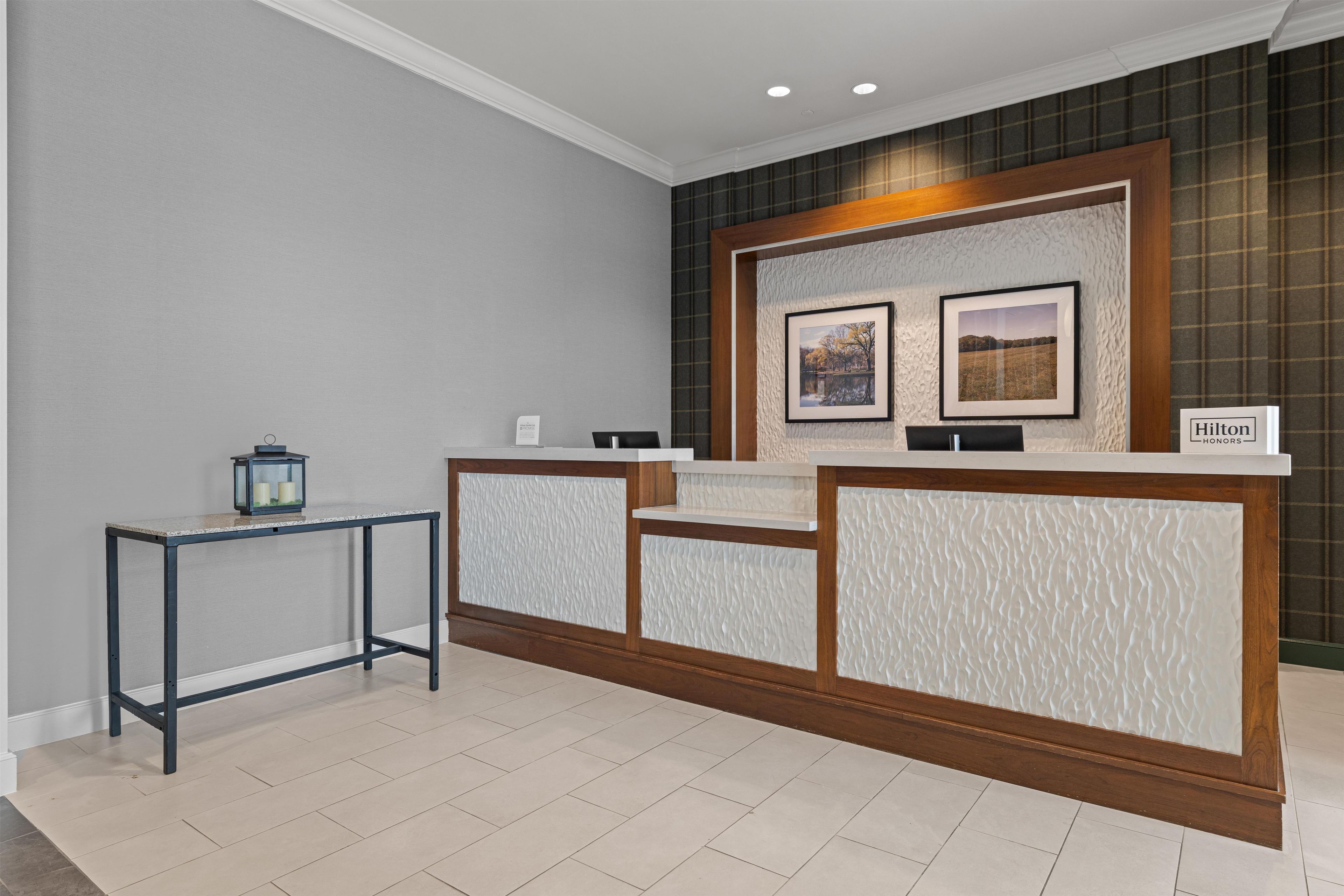 A reception desk with a modern design, two framed pictures on the wall, and a sign indicating Hilton Honors.