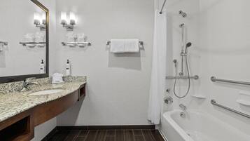 A bathroom with a granite countertop sink, a mirror, a shower with a handheld showerhead, and a bathtub.