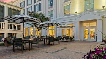 An outdoor patio area with tables and chairs, umbrellas, and potted plants.