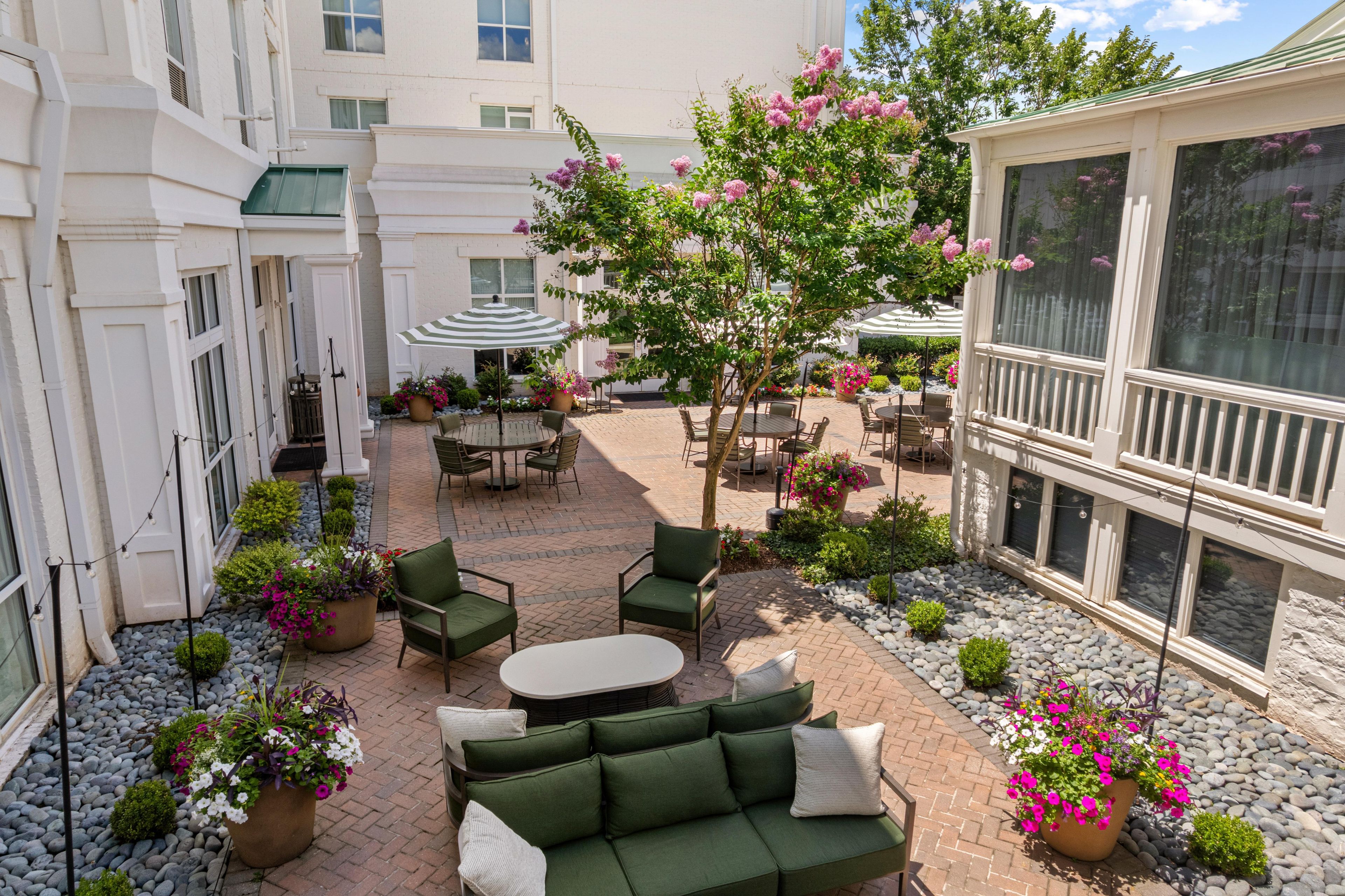 A courtyard with outdoor seating, a dining area, and a building with large windows.