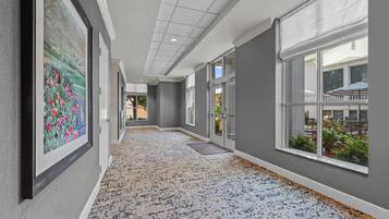Un couloir doté d’un tapis à motifs, de grandes fenêtres et d’une porte donnant sur un espace extérieur.
