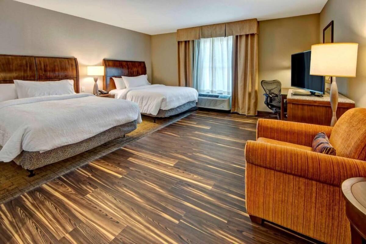 Une chambre d’hôtel avec deux lits, un canapé, une télévision et un bureau avec une lampe.