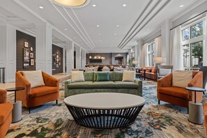 Eine großzügige Lobby mit einem grünen Sofa, orangefarbenen Sesseln, einem Couchtisch in der Mitte und einem gemusterten Teppich.