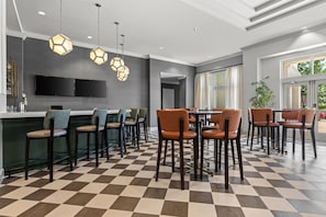 Un área de bar moderna con suelo a cuadros, iluminación colgante hexagonal y un televisor de pantalla plana en la pared.