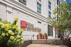 Un Hilton Garden Inn con fachada de ladrillo blanco, un logotipo rojo y escalones que conducen a la entrada.