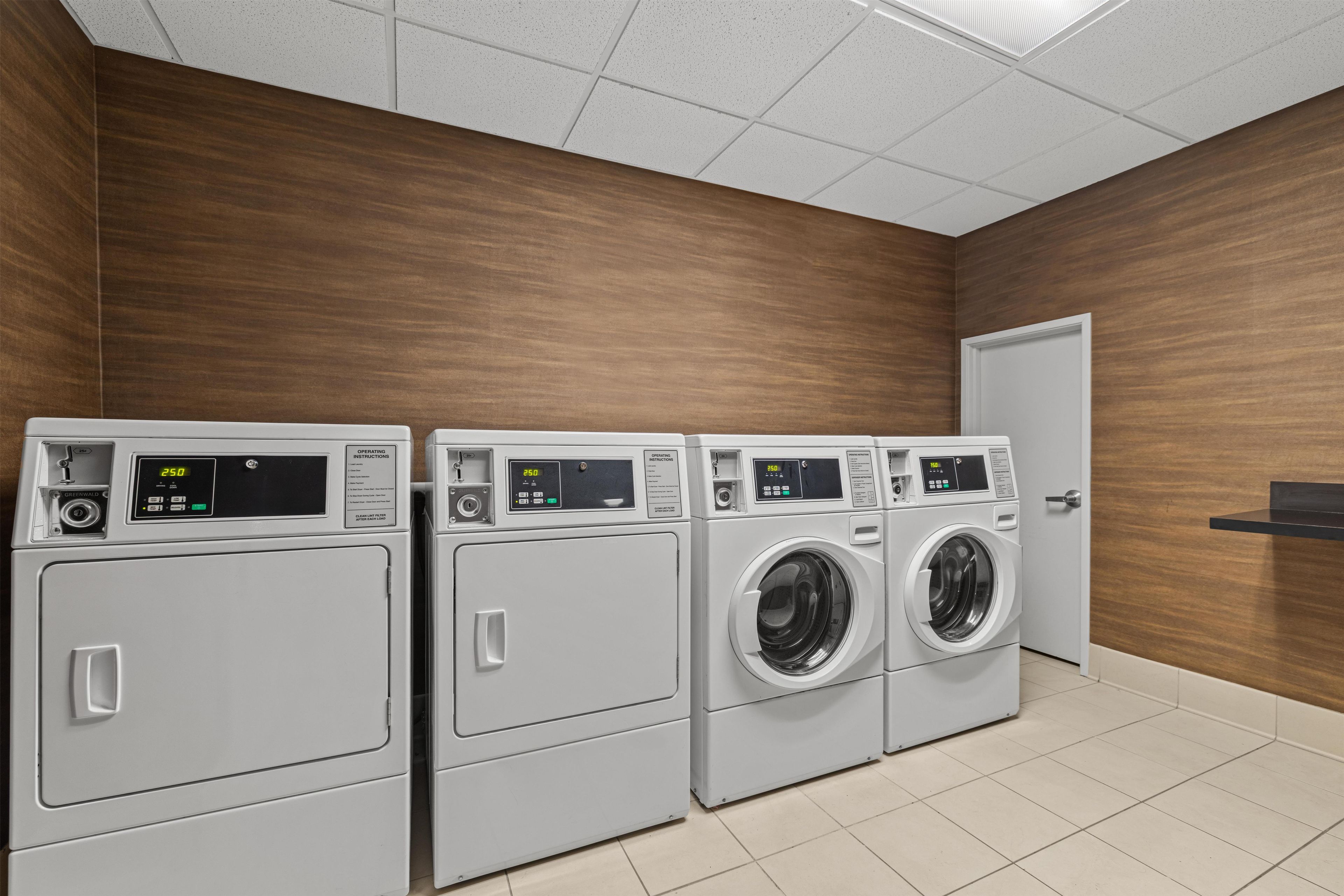A laundry room with four washing machines, a door, and wooden walls.