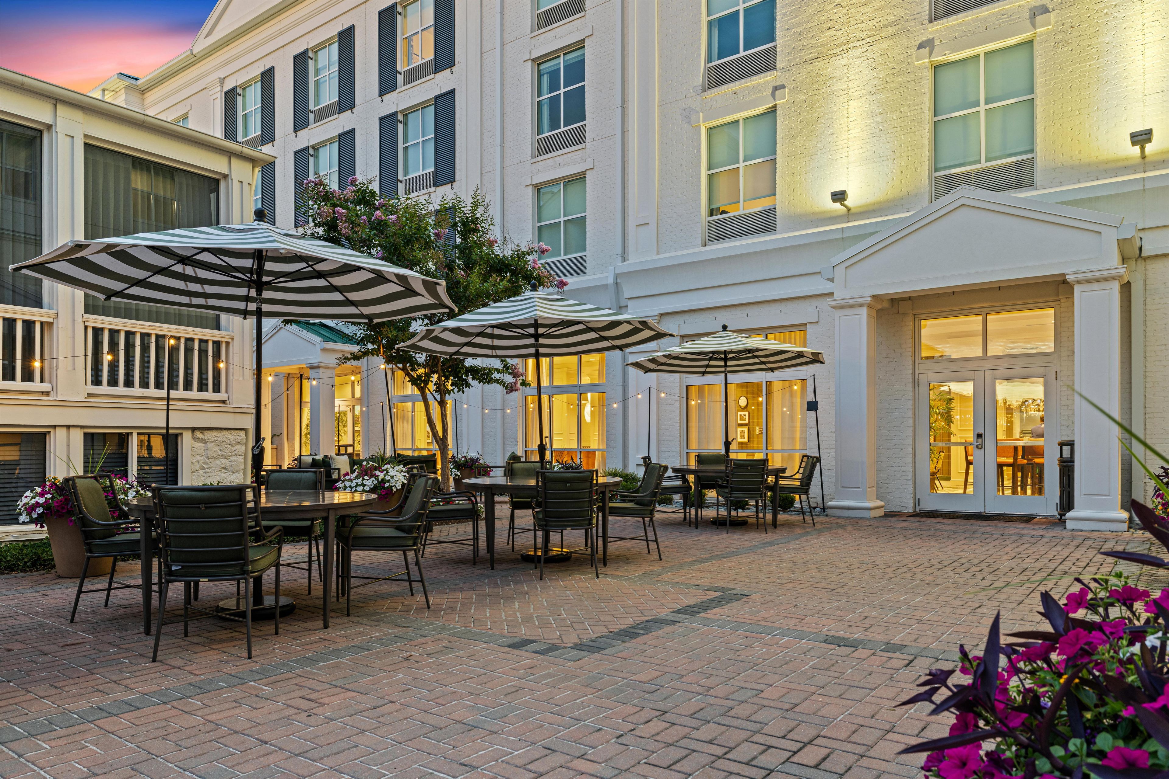 An outdoor patio area with tables and chairs, umbrellas, and potted plants.