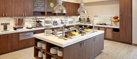 A modern kitchen with wooden cabinets, a marble countertop, and a central island with a food display.