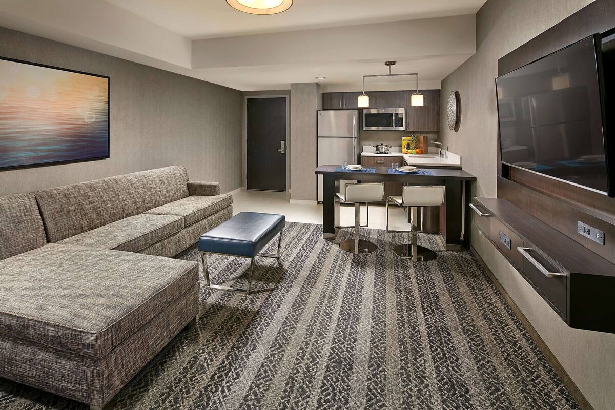 A modern living room with a sofa, ottoman, and a patterned rug.